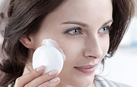 Frau reinigt Gesicht mit Wattepad.