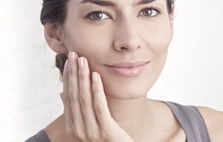 Frau trägt Creme im Gesicht auf.